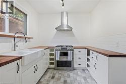Modern kitchen featuring white shaker-style cabinetry, wood-finish countertops, subway tile backsplash, a stainless steel range with a professional hood, and a farmhouse-style sink with a gooseneck fa - 