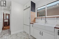 Kitchen featuring a large white farmhouse sink, white subway tile backsplash, and light wood-finish countertops - 