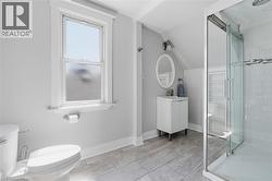 Contemporary bathroom featuring wood-finish tile flooring, a glass-enclosed shower, a white vanity with an oval mirror, and a window with white trim - 
