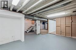 Expansive basement area with gray painted concrete flooring, exposed ceiling joists, and a white painted staircase - 