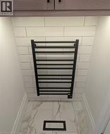 Matte black towel warmer against subway tile, complemented by wood-finish cabinetry, under-cabinet lighting, and large format tile flooring - 