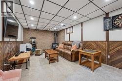 Finished basement space featuring recessed lighting, a drop ceiling, and a brick accent wall with a wood-burning stove - 