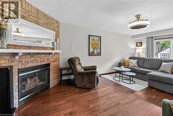 Living room featuring wood-finish flooring, a brick fireplace with a white mantel, and a built-in light fixture - 