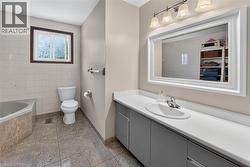 Bathroom featuring a built-in bathtub with tiled surround, a white toilet, and tile flooring - 