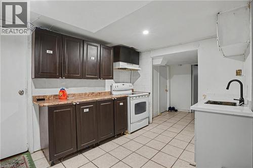 Kitchen area featuring dark wood-finish cabinetry, a white electric range, a white countertop with an undermount sink and a matte black gooseneck faucet, and square tile flooring - 47 Bowman Street, Hamilton, ON - Indoor Photo Showing Kitchen