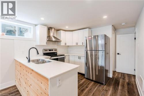 Modern kitchen featuring white shaker cabinetry, stainless steel appliances, a wood-paneled island with an undermount double sink, white countertops, and wood-finish flooring - 16 Ronaldshay Avenue, Hamilton, ON - Indoor Photo Showing Kitchen With Double Sink