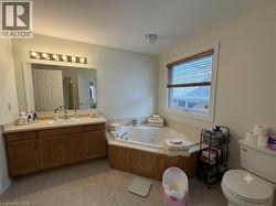Bathroom featuring a corner jetted tub with wood-finish paneling, a single vanity with a solid surface countertop, and a large wall mirror - 