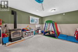 Spacious room featuring a central wood-burning stove with a black stovepipe, light-toned carpeting, and a window with white blinds - 