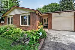 Brick exterior with a peaked roofline, an attached garage, a front entry with an oval glass insert, and a landscaped garden bed - 