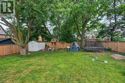 Expansive fenced backyard featuring a manicured lawn, mature trees, and a storage shed - 
