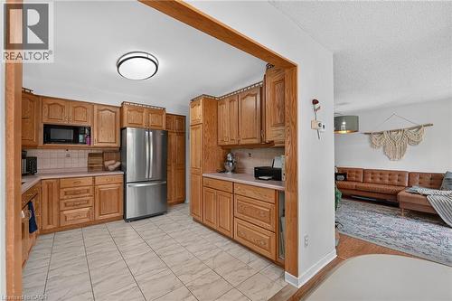Kitchen featuring wood cabinetry, tile flooring, stainless steel refrigerator, built-in microwave, and solid surface countertops - 3 Orchard Parkway, Grimsby, ON - Indoor Photo Showing Kitchen