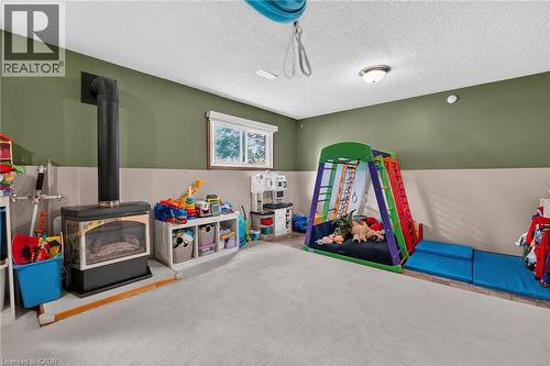 Spacious room featuring a central wood-burning stove with a black stovepipe, light-toned carpeting, and a window with white blinds - 3 Orchard Parkway, Grimsby, ON - Indoor Photo Showing Other Room