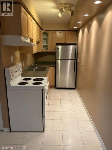 Compact kitchen featuring light wood cabinetry, a stainless steel refrigerator, and a white electric range - 30 Summit Avenue Unit# 604, Hamilton, ON - Indoor Photo Showing Kitchen