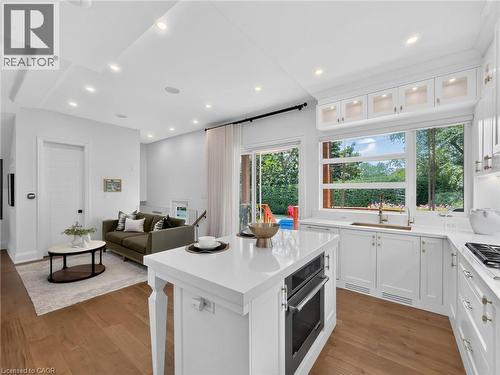 Open-concept kitchen featuring an integrated oven, white cabinetry with gold-tone hardware, a large window overlooking green foliage, and wood-finish flooring - 5178 Hunter Drive, Burlington, ON - Indoor Photo Showing Kitchen With Upgraded Kitchen
