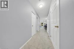 Hallway featuring light-toned tile flooring, light gray wall paint, white trim, and recessed lighting - 