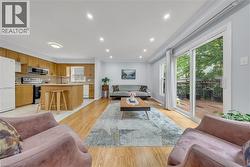Open-concept living space featuring wood-finish flooring throughout, a kitchen with natural wood cabinetry and stainless steel appliances, a center island with seating, recessed lighting, and sliding - 