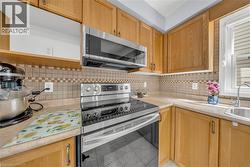 Kitchen featuring wood cabinetry, stainless steel appliances including a range and microwave, light-toned countertops, a tile backsplash, and an undermount sink - 