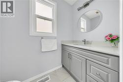 Bathroom featuring a single window, a light gray vanity with a white countertop, an oval mirror, and a wall-mounted light fixture - 