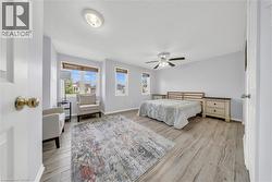 Spacious room featuring wood-finish flooring, multiple windows with blinds, a ceiling fan with integrated lighting, and neutral wall tones - 