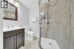 Curved glass shower enclosure with tiled walls, dark wood-finish vanity with white countertop and integrated sink, chrome faucet, and overhead vanity lighting - 