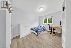 Bedroom featuring wood-finish flooring, a white trim window, a ceiling-mounted light fixture, and light-toned wall paint - 