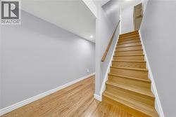 Hardwood staircase with natural wood handrail, light gray walls, white trim, recessed lighting, and wood-finish flooring - 