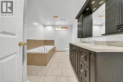 Bathroom featuring a long built-in tub with tile surround, a dark wood vanity with a light-colored countertop, and integrated lighting above the mirror - 