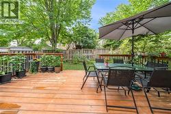 Expansive wooden deck featuring a perimeter railing, offering access to a green lawn area with mature trees and a wooden privacy fence - 