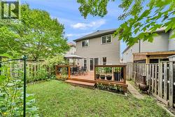 Expansive backyard featuring a wood-finish deck with railing, a grass lawn, and mature trees providing natural shading - 