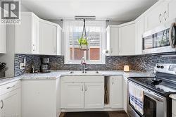 Bright kitchen featuring white cabinetry, a mosaic tile backsplash, granite-finish countertops, stainless steel appliances, and a double basin sink beneath a window - 