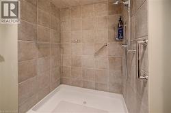 Walk-in shower featuring neutral-toned tile walls, a white shower pan, a wall-mounted showerhead, and chrome grab bars - 