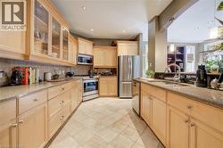 Kitchen featuring wood cabinetry, stainless steel appliances, granite countertops, tile backsplash, and tile flooring - 