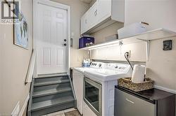 Dedicated utility area featuring a paneled door, built-in shelving, under-cabinet lighting, upper cabinetry, and a washer and dryer - 
