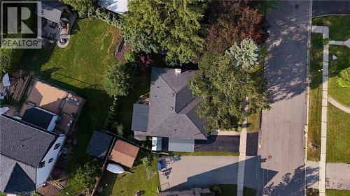 Aerial view showcasing a residential property with a dark grey shingle roof, mature trees, and a paved driveway leading to a single-story structure - 11 Summit Crescent, Guelph, ON - Outdoor With View