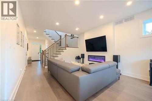 Open-concept living area featuring light wood-finish flooring, recessed lighting, a modern electric fireplace, and a contemporary staircase with wood treads and metal balusters - 9 Princeton Common, St. Catharines, ON - Indoor With Fireplace