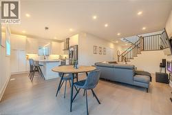 Open concept living area featuring wood-finish flooring, recessed lighting, and a contemporary staircase with dark wood handrails and black metal spindles - 