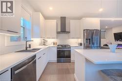 Modern kitchen featuring white flat-panel cabinetry, light-toned countertops, a stainless steel gas range with coordinating vent hood, and a deep undermount sink with a matte black faucet - 