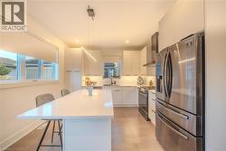 Modern kitchen featuring a large island with seating, stainless steel appliances, white cabinetry, and wood-finish flooring - 