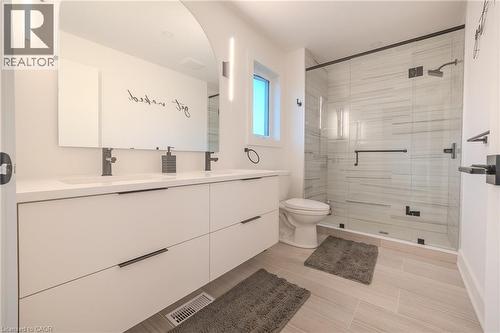 Contemporary bathroom featuring a spacious dual-sink vanity with matte black hardware, an arched frameless mirror, and modern vertical sconces - 9 Princeton Common, St. Catharines, ON - Indoor Photo Showing Bathroom