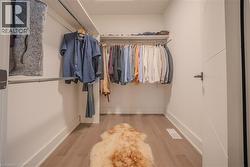 Walk-in closet featuring light wood-finish flooring, white walls, and built-in metal hanging rods - 