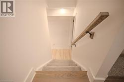 Staircase featuring wood-finish treads and risers, carpeted steps, a wood-finish handrail with black iron brackets, and white wall finishes - 