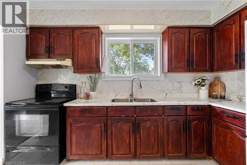 Kitchen featuring wood-finish cabinetry, a black electric range, a double basin stainless steel sink, and white countertops with a matching backsplash - 383 Bartley Bull Parkway, Brampton, ON - Indoor Photo Showing Kitchen With Double Sink