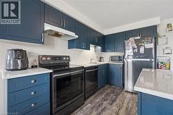 Kitchen featuring navy blue cabinetry with brushed nickel hardware, white countertops, and wood-finish flooring - 