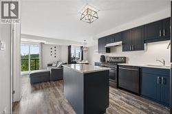 Open-concept living area featuring a kitchen with navy cabinetry, light countertops, and black stainless steel appliances - 