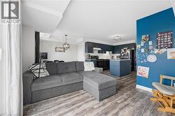 Open-concept living area featuring wood-finish flooring, a contemporary kitchen with dark cabinetry and black appliances, a central island, and recessed lighting - 