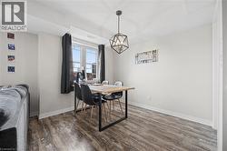 Dining area featuring wood-finish flooring, a geometric pendant light fixture, and a large window with dark drapery - 