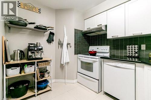 Compact kitchen featuring white cabinetry, a built-in range hood, a tile backsplash, black countertops, and a white oven - 175 Hunter Street E Unit# 103, Hamilton, ON - Indoor Photo Showing Kitchen