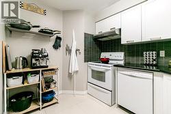 Compact kitchen featuring white cabinetry, a built-in range hood, a tile backsplash, black countertops, and a white oven - 