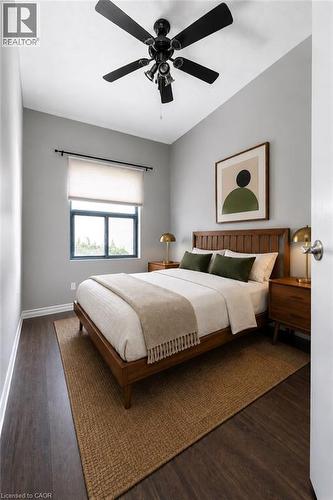 Bedroom featuring dark wood-finish flooring, a contemporary window with a roller shade, and a black ceiling fan with integrated lighting - 175 Hunter Street E Unit# 103, Hamilton, ON - Indoor Photo Showing Bedroom