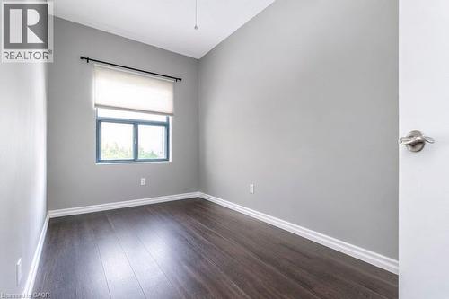 Room featuring wood-finish flooring, light grey walls, white baseboards, and a window with a roller shade - 175 Hunter Street E Unit# 103, Hamilton, ON - Indoor Photo Showing Other Room